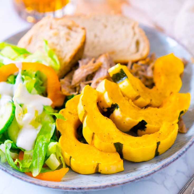 roasted delicata squash on blue plate with salad, bread slices, and pulled pork